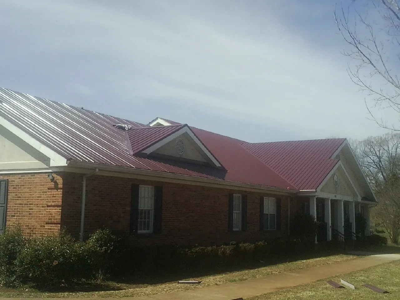 Red metal roof with gabled entries on a long brick building, from a Hail Damage Roof Repair job in Wills Point