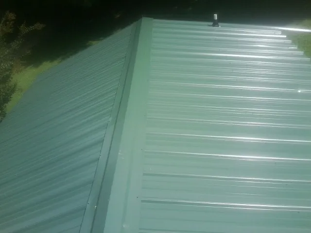 New green metal panels meeting at the ridge of a roof — Flat Roof Repair work by our crew in Wills Point