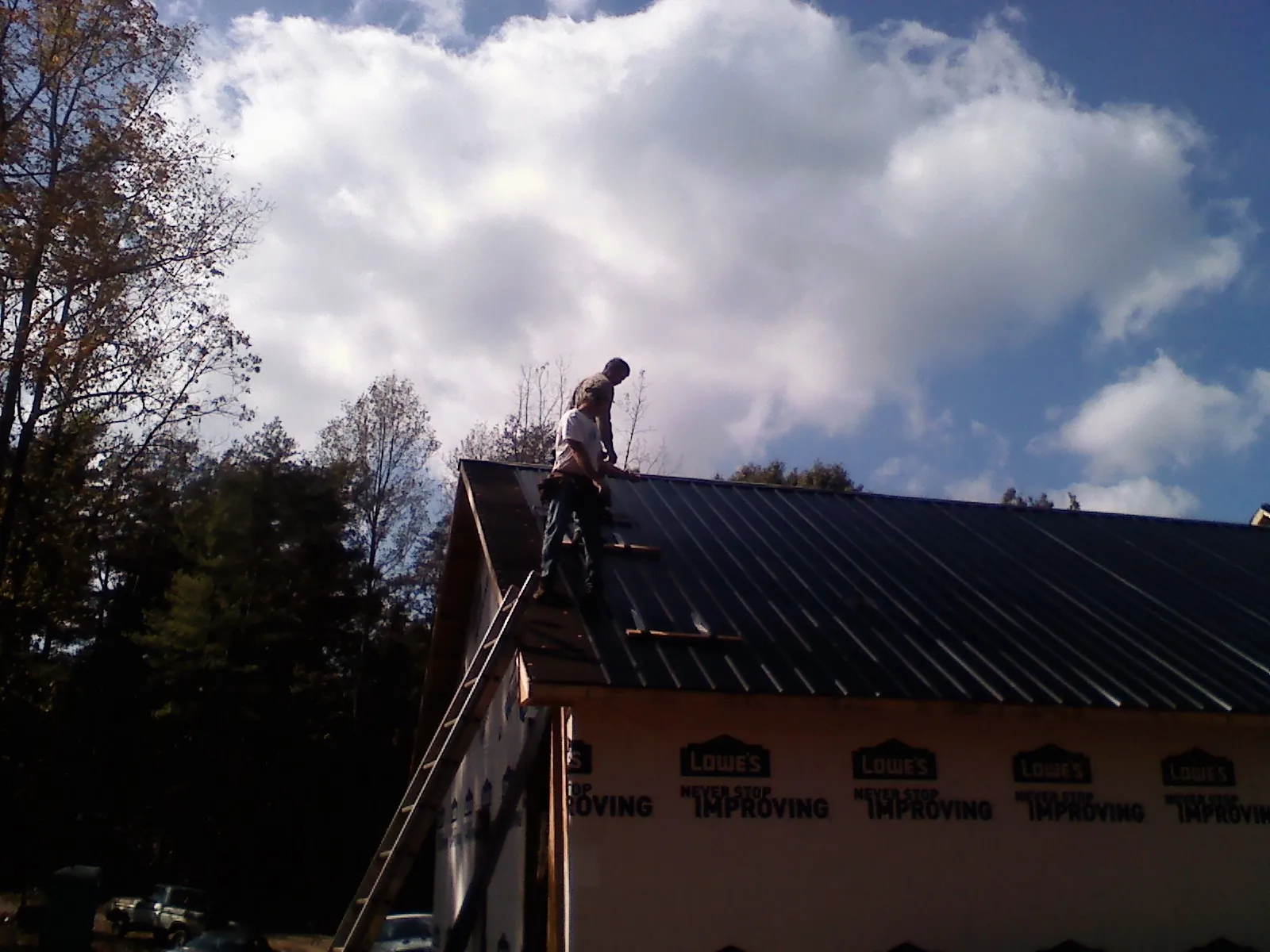 Roofer fastening dark metal panels high against a cloudy sky, from a Roof Inspection job in Wills Point