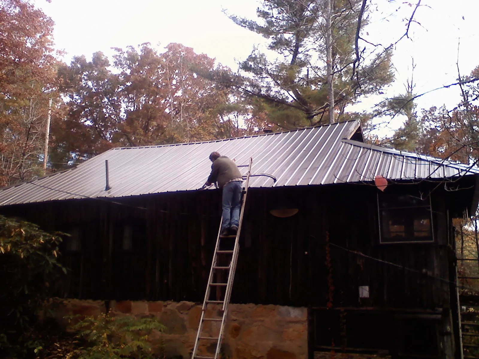 Roofer on a ladder working along the edge of a cabin metal roof in Wills Point