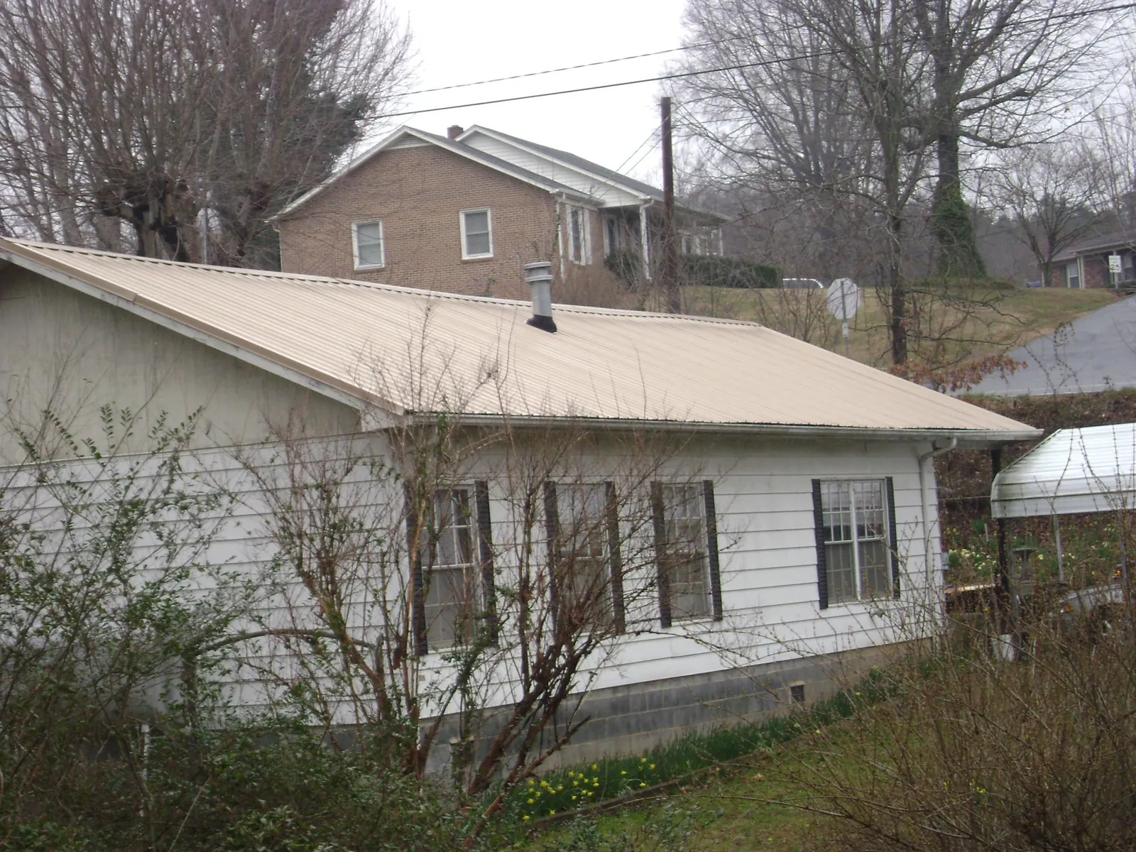 Tan metal roof on a white sided house set into a hillside — Commercial Roofing by Roofing Brothers in Wills Point