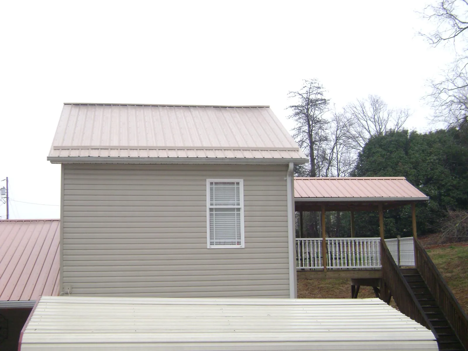 Tan metal roofs on a two story addition and attached porch, from a Roof Replacement job in Wills Point